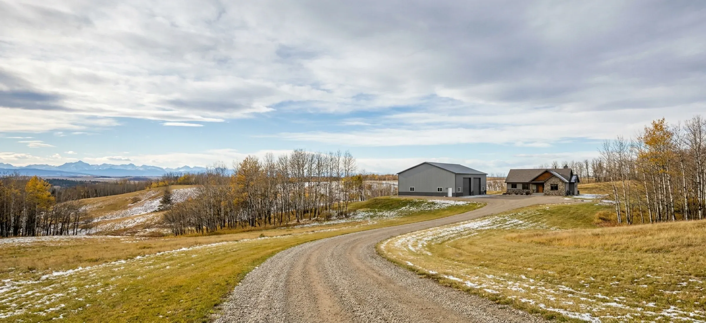 Hilly acreage land with aspen groves, a steel shop and a gravel drive, mountains in the distance