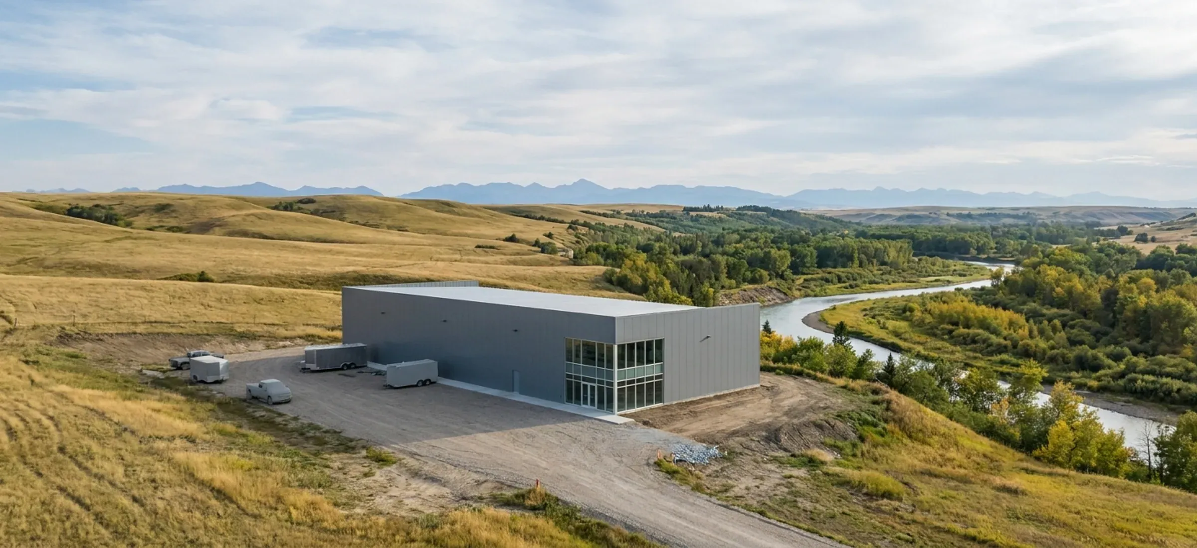 A steel building in a business park near a treed river valley, rolling foothills to the west