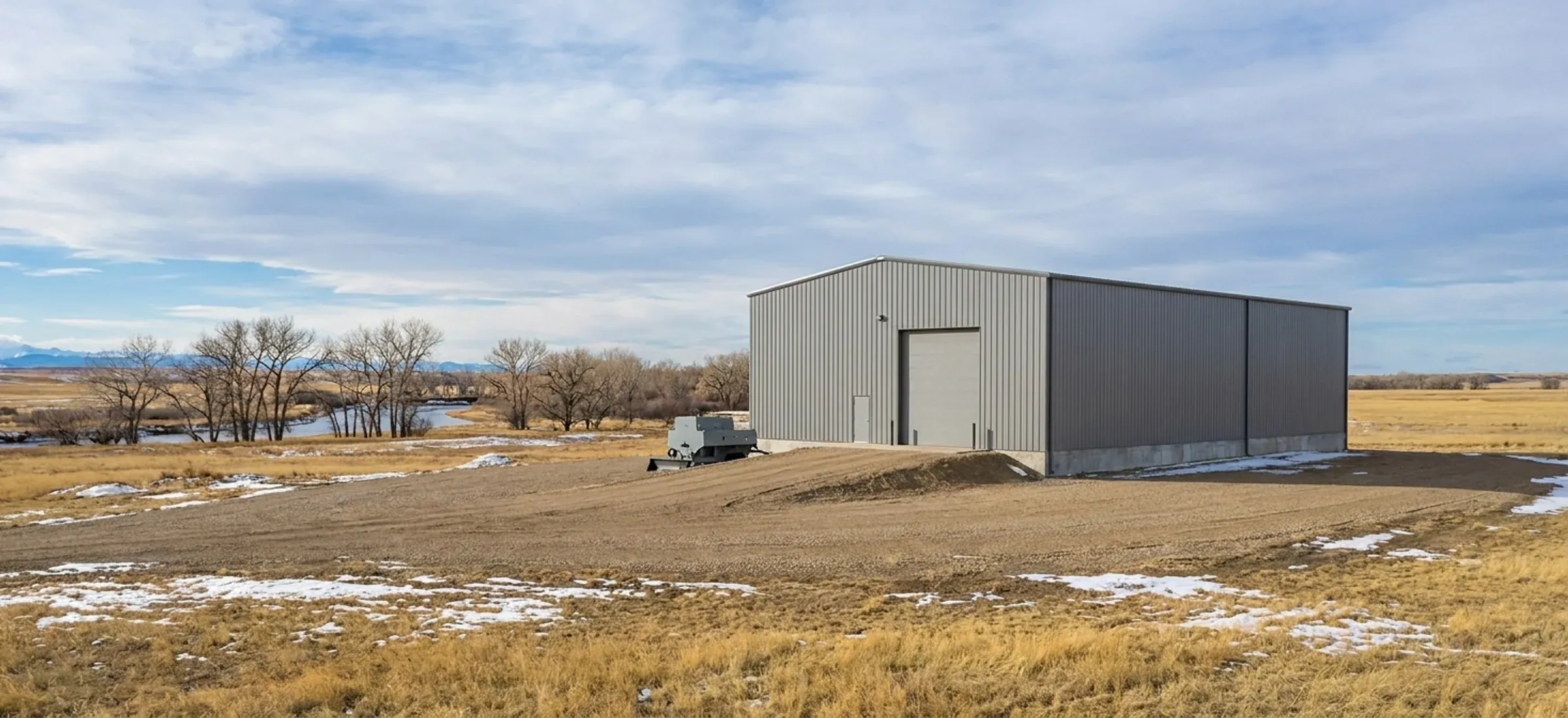 A steel shop building with a raised floor on an elevated pad, prairie and mountains beyond